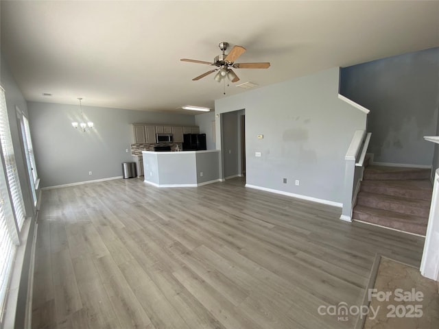 unfurnished living room with light wood-style floors, baseboards, and ceiling fan with notable chandelier