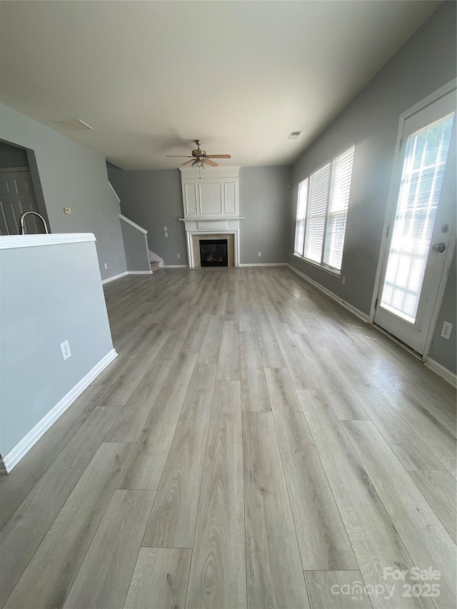 unfurnished living room featuring baseboards, light wood finished floors, ceiling fan, visible vents, and a fireplace