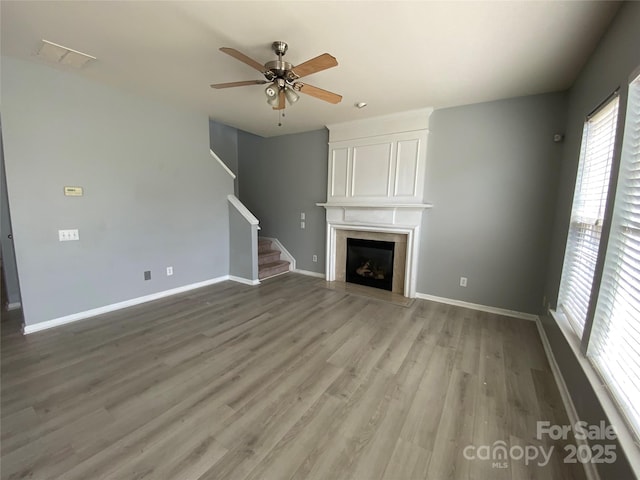 unfurnished living room with light wood-type flooring, stairs, baseboards, and a ceiling fan