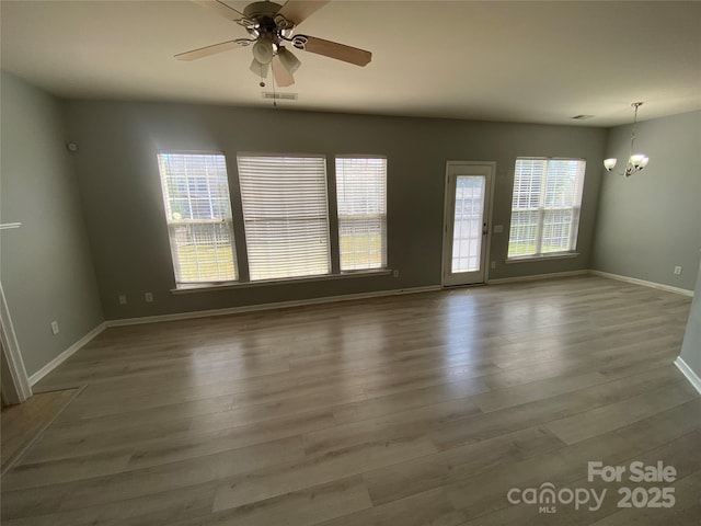 spare room featuring ceiling fan with notable chandelier, baseboards, visible vents, and wood finished floors
