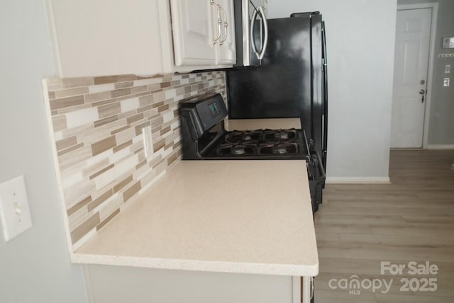 10901 Claude Freeman Dr, Charlotte, NC 28262 - kitchen with gas stove, light wood-style floors, white cabinets, baseboards, and backsplash