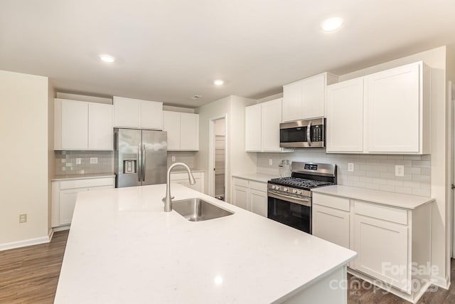 kitchen featuring stainless steel appliances, a sink, decorative backsplash, dark wood finished floors, and a kitchen island with sink