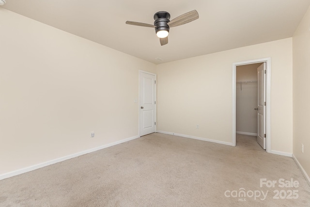 unfurnished bedroom with light carpet, baseboards, a spacious closet, and a ceiling fan
