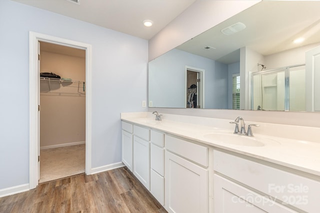 full bath featuring a shower stall, double vanity, wood finished floors, baseboards, and a walk in closet