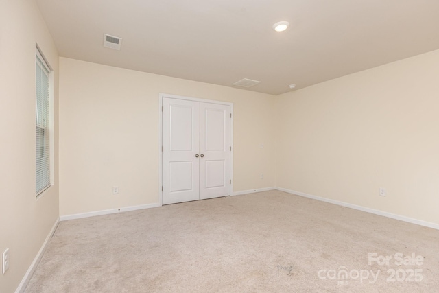 spare room featuring light colored carpet and baseboards