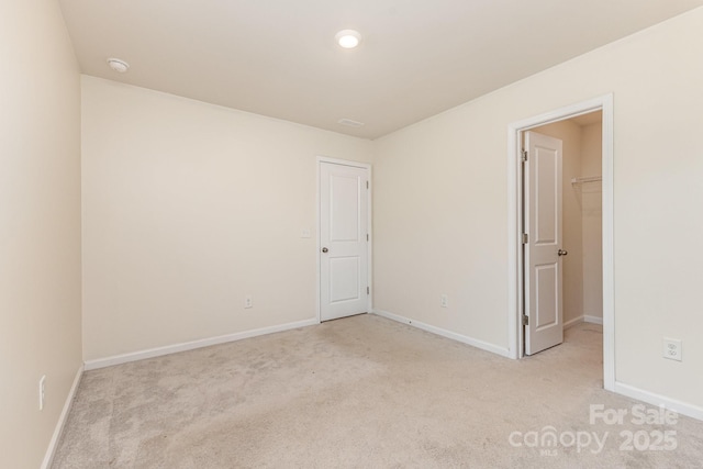 unfurnished bedroom with light carpet, a walk in closet, baseboards, and recessed lighting