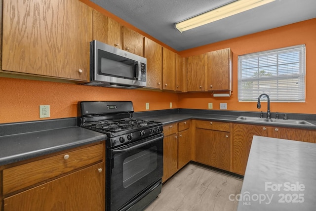 kitchen with stainless steel microwave, black range with gas cooktop, a sink, and brown cabinets