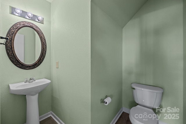 half bathroom with toilet, baseboards, wood finished floors, and vaulted ceiling