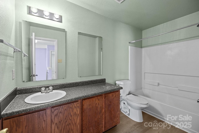 bathroom featuring toilet, wood finished floors, vanity, shower / bathtub combination, and a textured wall