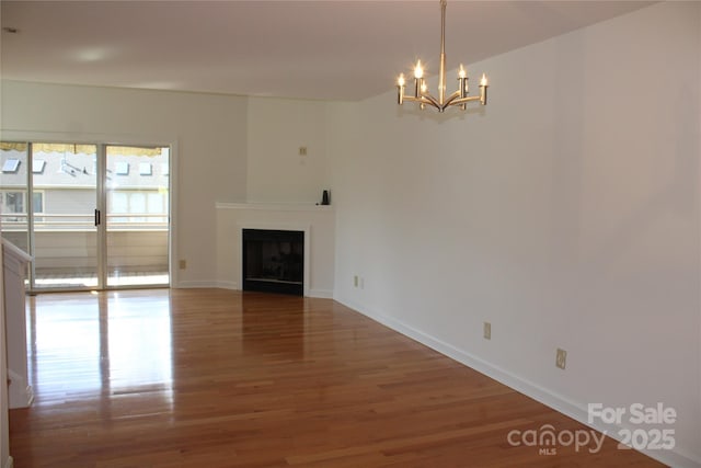 unfurnished living room with a fireplace, an inviting chandelier, baseboards, and wood finished floors