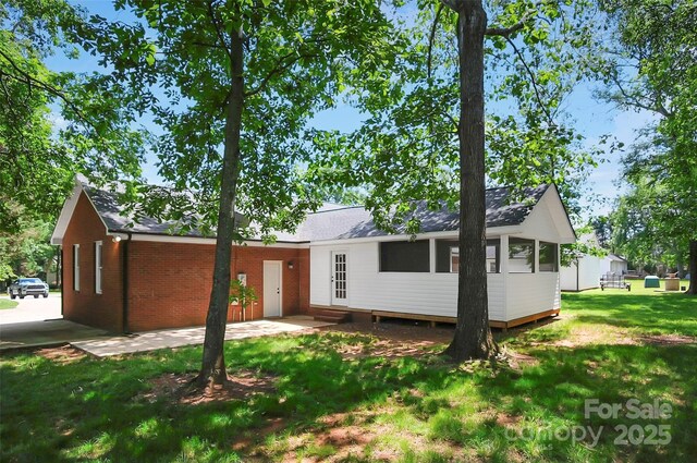 back of house featuring a lawn, roof with shingles, and brick siding