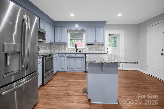kitchen with appliances with stainless steel finishes, a sink, light stone countertops, tasteful backsplash, and light wood-style flooring