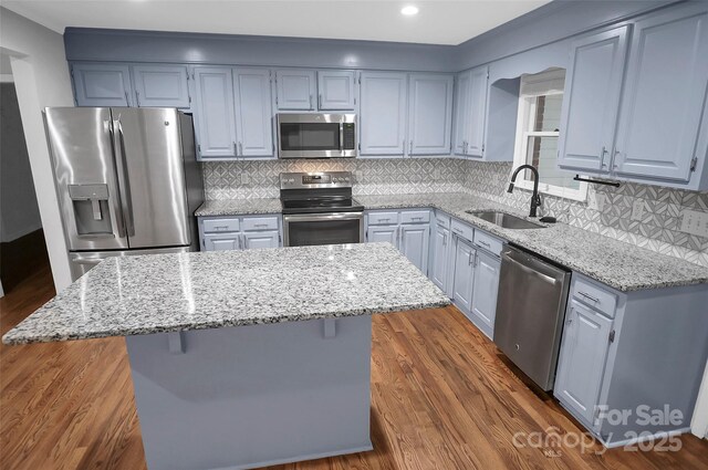 kitchen featuring appliances with stainless steel finishes, a sink, light stone countertops, a kitchen island, and dark wood finished floors