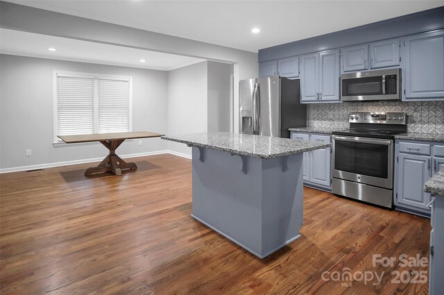 kitchen with appliances with stainless steel finishes, light stone countertops, tasteful backsplash, a center island, and a breakfast bar area