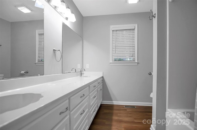 full bath featuring wood finished floors, double vanity, baseboards, and toilet