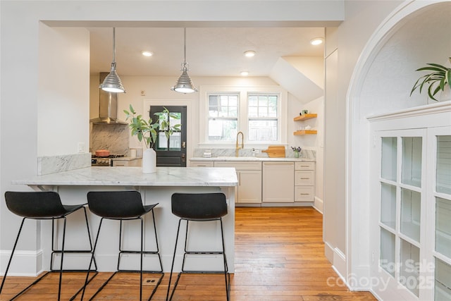 118 Macon Ave, Asheville, NC 28801 - kitchen featuring a breakfast bar, a peninsula, wall chimney range hood, light stone counters, and a sink