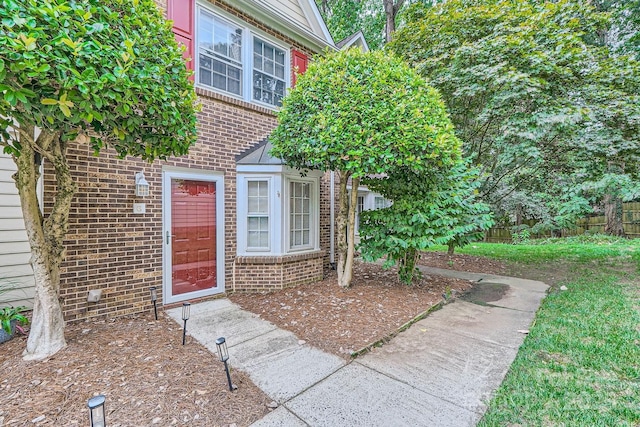 view of exterior entry with brick siding and fence