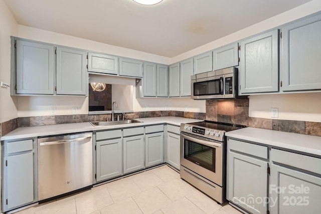 kitchen with appliances with stainless steel finishes, a sink, light tile patterned flooring, gray cabinetry, and light countertops