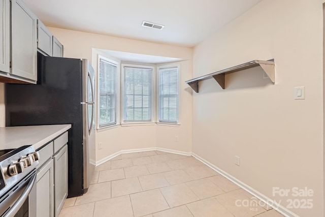 kitchen with stainless steel gas range oven, light countertops, baseboards, light tile patterned flooring, and gray cabinets