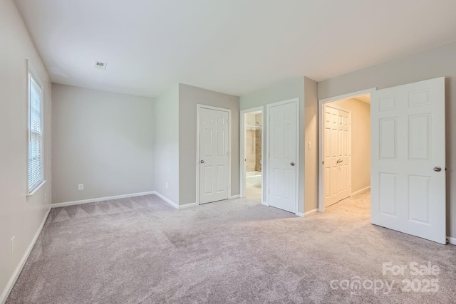 unfurnished bedroom featuring light carpet, ensuite bathroom, and baseboards