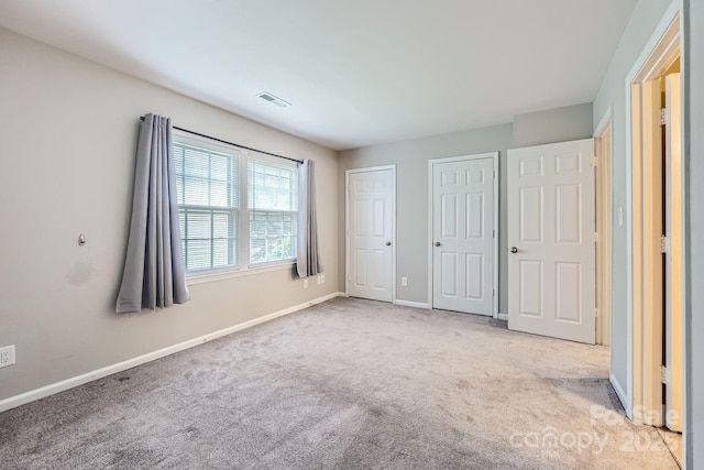 unfurnished bedroom with two closets, carpet floors, and baseboards