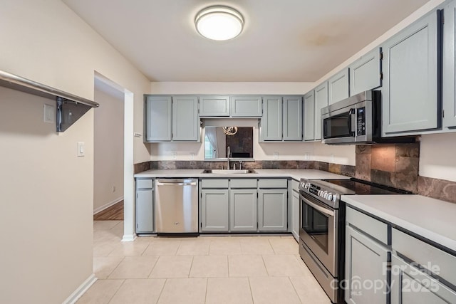 kitchen with appliances with stainless steel finishes, a sink, light tile patterned flooring, baseboards, and gray cabinetry