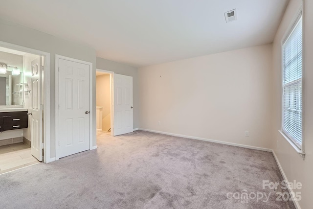 unfurnished bedroom with light colored carpet, ensuite bath, and baseboards