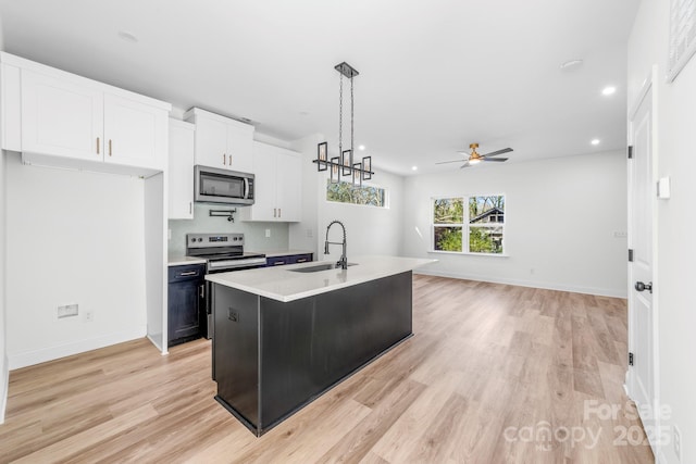 kitchen featuring stainless steel appliances, a sink, light countertops, light wood finished floors, and a ceiling fan