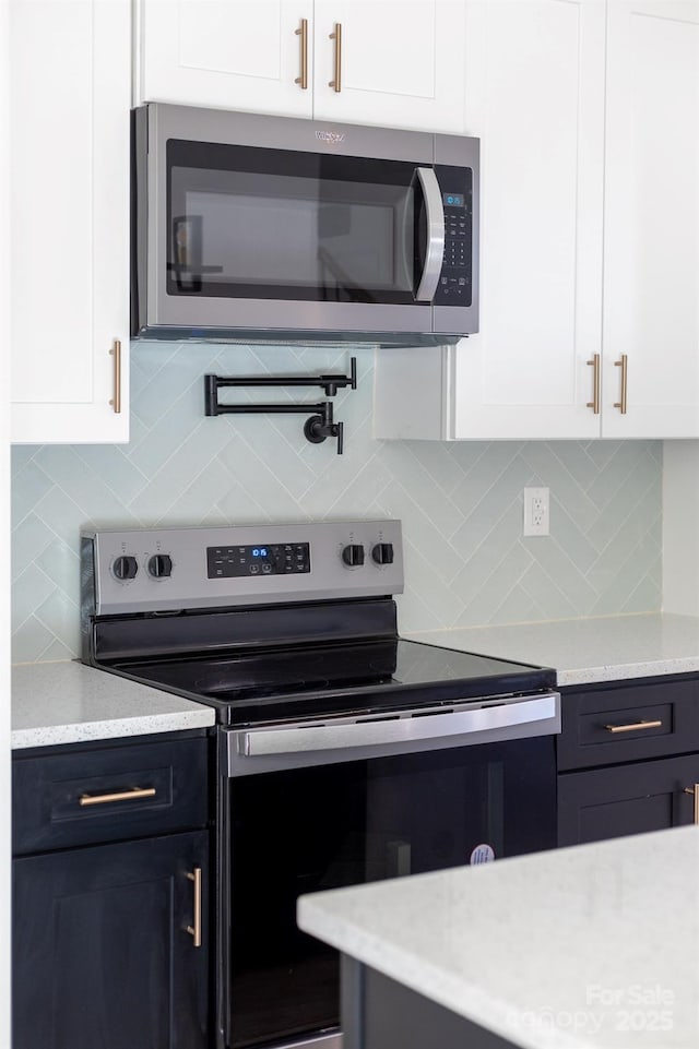 kitchen featuring appliances with stainless steel finishes, white cabinets, backsplash, and light stone countertops