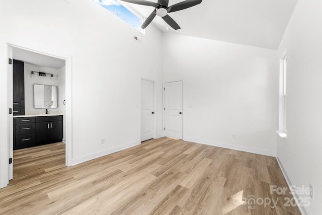 unfurnished bedroom featuring high vaulted ceiling, baseboards, light wood finished floors, ensuite bath, and a sink