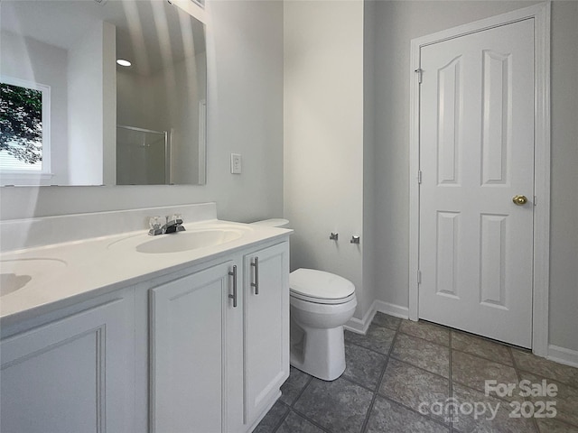 bathroom with toilet, baseboards, a shower with shower door, a sink, and double vanity