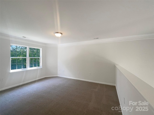spare room with visible vents, baseboards, ornamental molding, and dark colored carpet