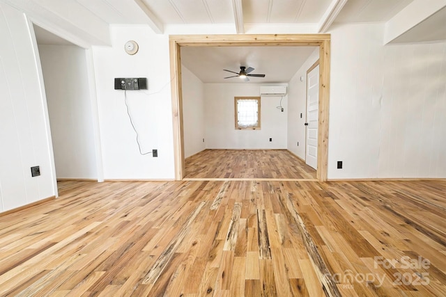 spare room with a wall mounted AC, baseboards, a ceiling fan, and light wood-style floors