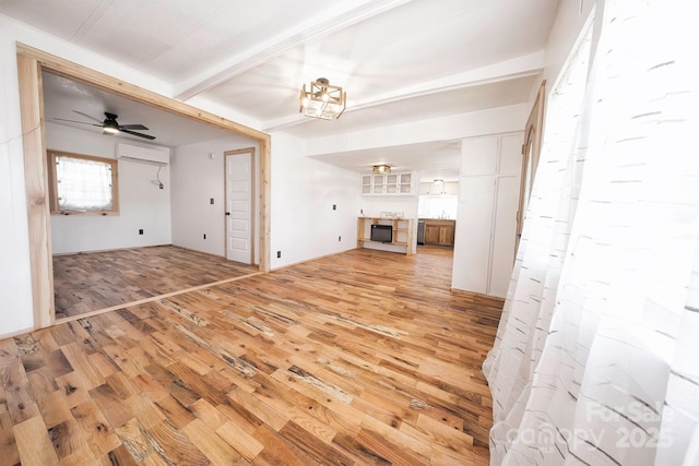 unfurnished living room with a wall mounted air conditioner, beamed ceiling, light wood-style flooring, and ceiling fan
