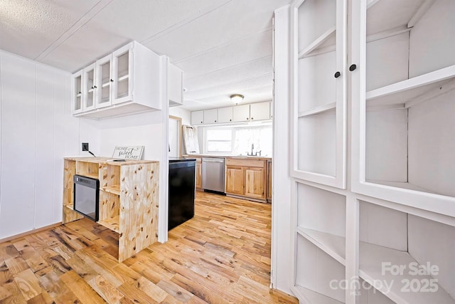 kitchen featuring glass insert cabinets, dishwasher, light wood finished floors, a sink, and light countertops