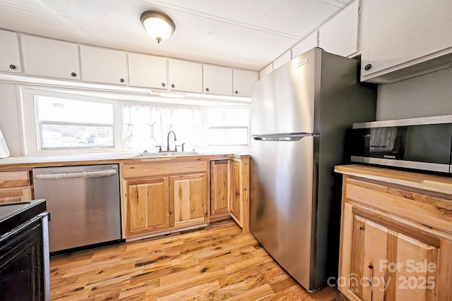 kitchen with a sink, stainless steel appliances, light countertops, white cabinets, and light wood-style floors