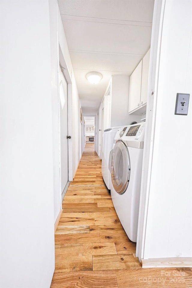 clothes washing area featuring cabinet space, washing machine and dryer, and light wood finished floors