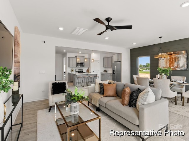 living room featuring light wood-style flooring, recessed lighting, baseboards, visible vents, and ceiling fan with notable chandelier