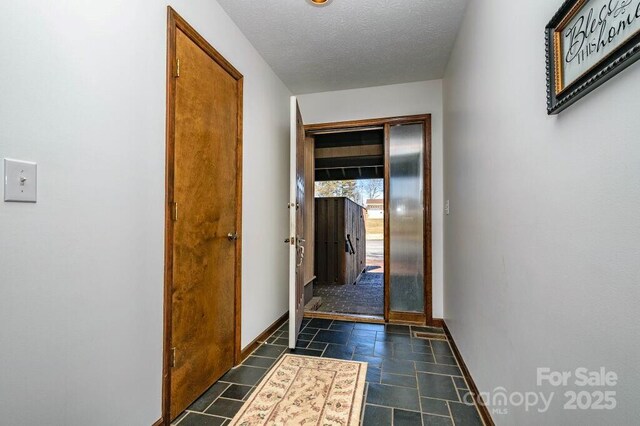 hallway with baseboards, a textured ceiling, and stone tile flooring