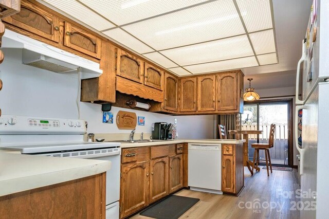kitchen with white appliances, brown cabinets, under cabinet range hood, light wood-style flooring, and light countertops