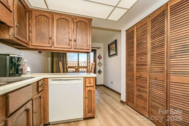 kitchen featuring dishwasher, light countertops, light wood finished floors, a peninsula, and brown cabinetry