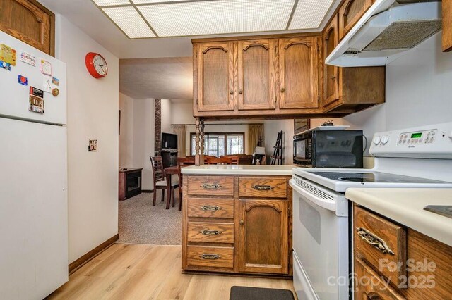 kitchen with white appliances, under cabinet range hood, brown cabinetry, a peninsula, and light countertops