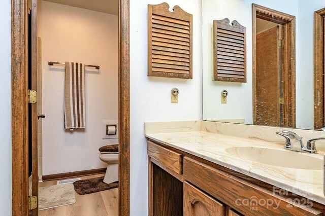 bathroom with toilet, wood finished floors, vanity, and baseboards