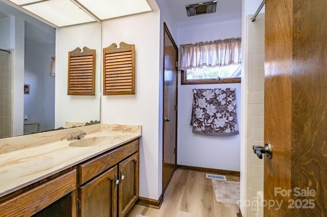 full bath with wood finished floors, vanity, a shower, and baseboards