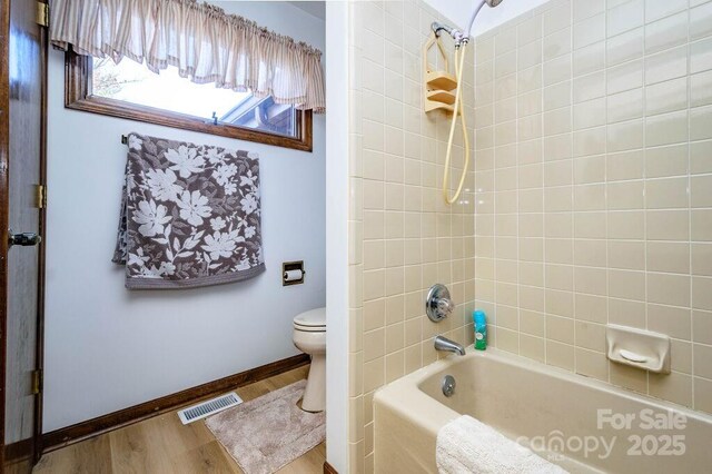 bathroom featuring toilet, wood finished floors, shower / washtub combination, and baseboards