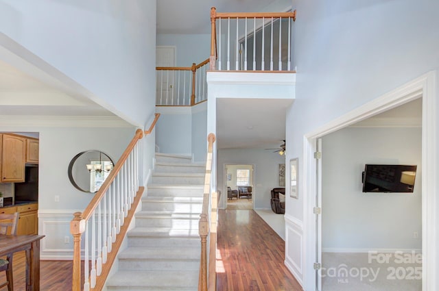 stairs featuring wood finished floors, a ceiling fan, crown molding, and a high ceiling