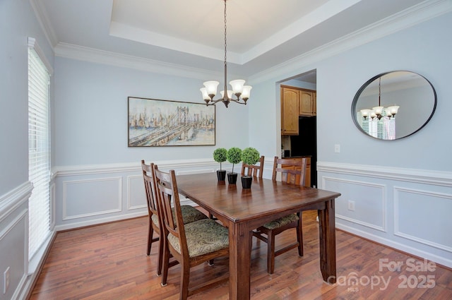 dining space with a chandelier, wood finished floors, a decorative wall, wainscoting, and a raised ceiling