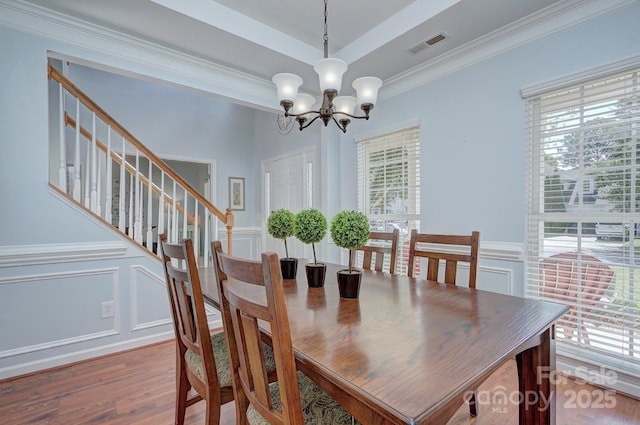 dining room featuring a decorative wall, a chandelier, wood finished floors, ornamental molding, and a wainscoted wall