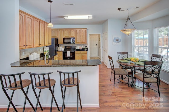 kitchen featuring black appliances, decorative backsplash, a breakfast bar, light brown cabinetry, and baseboards