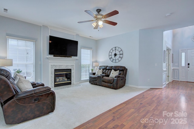 living area featuring healthy amount of natural light, a ceiling fan, wood finished floors, and a high end fireplace